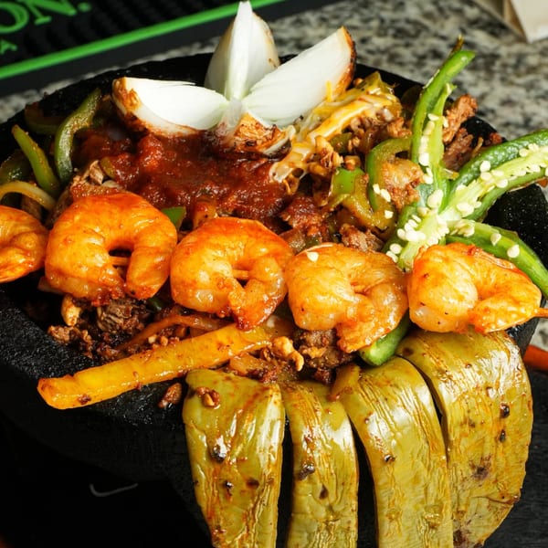 A sizzling molcajete dish with shrimp, steak, onions, bell peppers, and jalapeños.