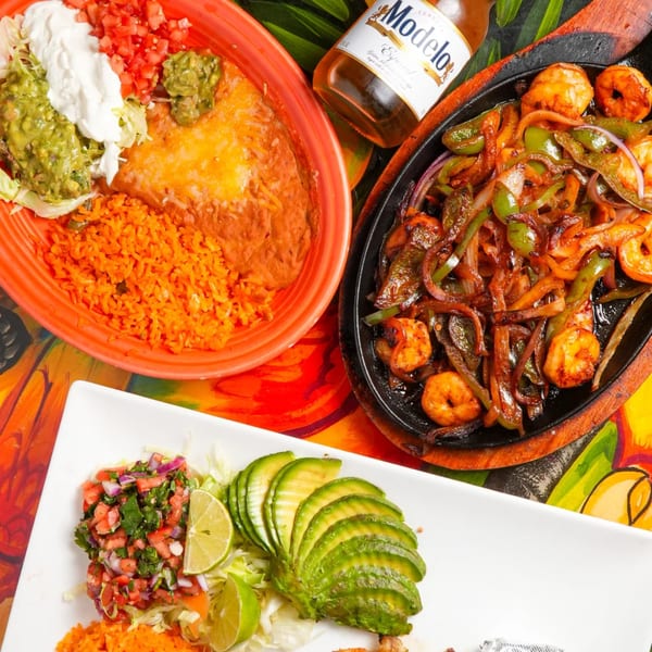 A vibrant Mexican feast with shrimp fajitas, enchiladas, rice, beans, guacamole, and a Modelo beer.