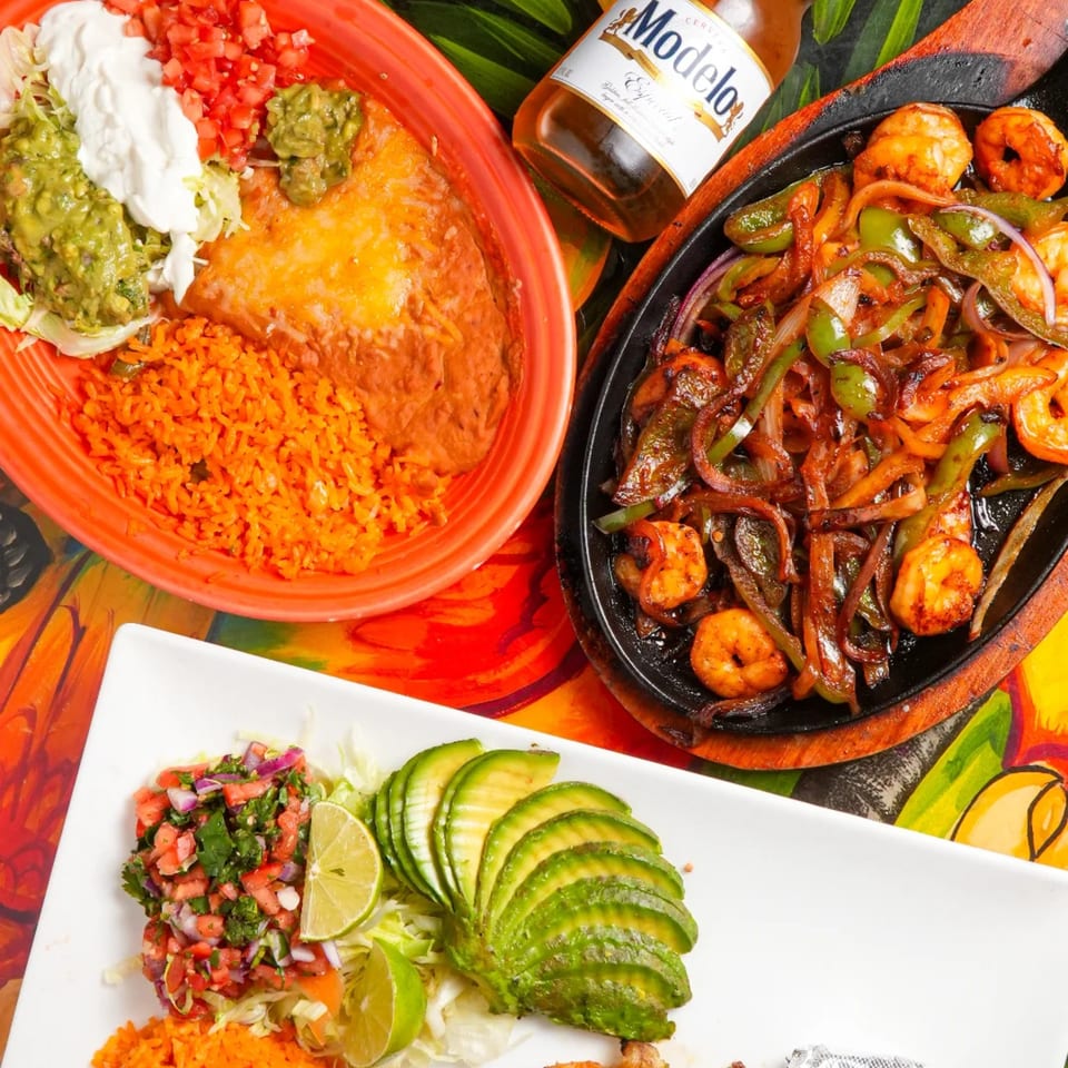 A vibrant Mexican feast with shrimp fajitas, enchiladas, rice, beans, guacamole, and a Modelo beer.