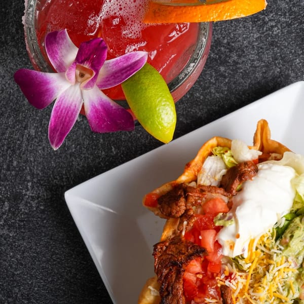 Overhead view of a Los Magueyes taco salad and a red margarita garnished with a lime and orchid.