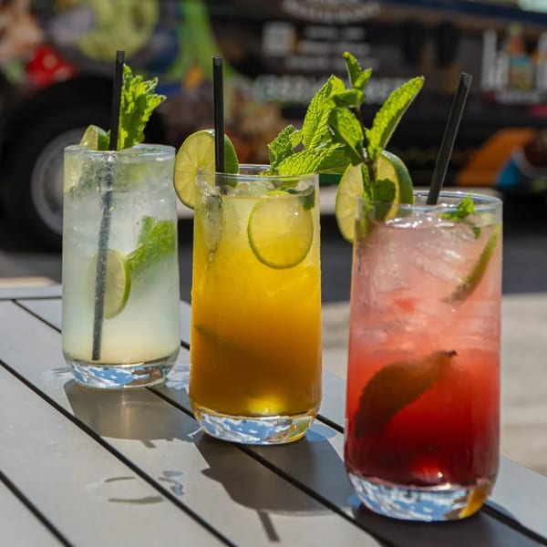 Three colorful mojitos, garnished with lime and mint, sit on an outdoor table at Los Magueyes.