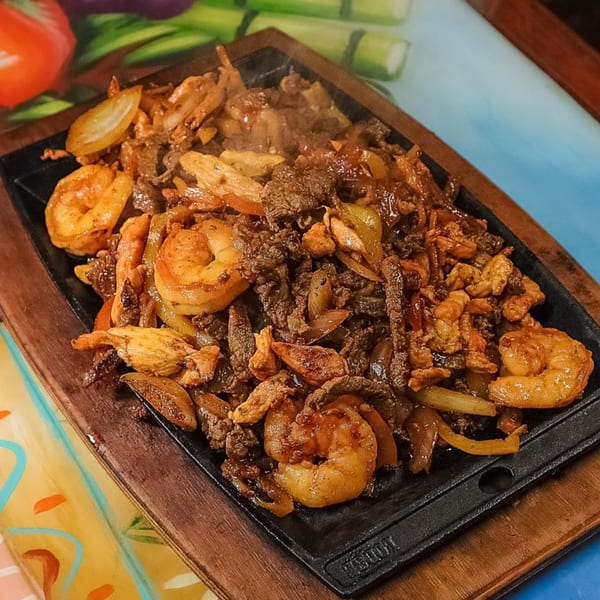 Sizzling fajitas with shrimp, beef, chicken, and onions on a hot cast iron platter.