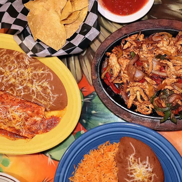 A vibrant spread of Mexican dishes, including fajitas, enchiladas, rice, beans, chips, and salsa.