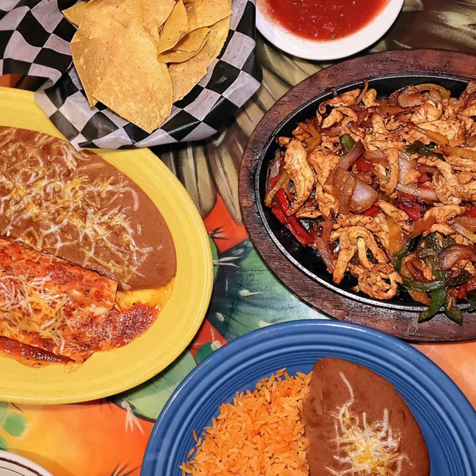 A vibrant spread of Mexican dishes, including fajitas, enchiladas, rice, beans, chips, and salsa.