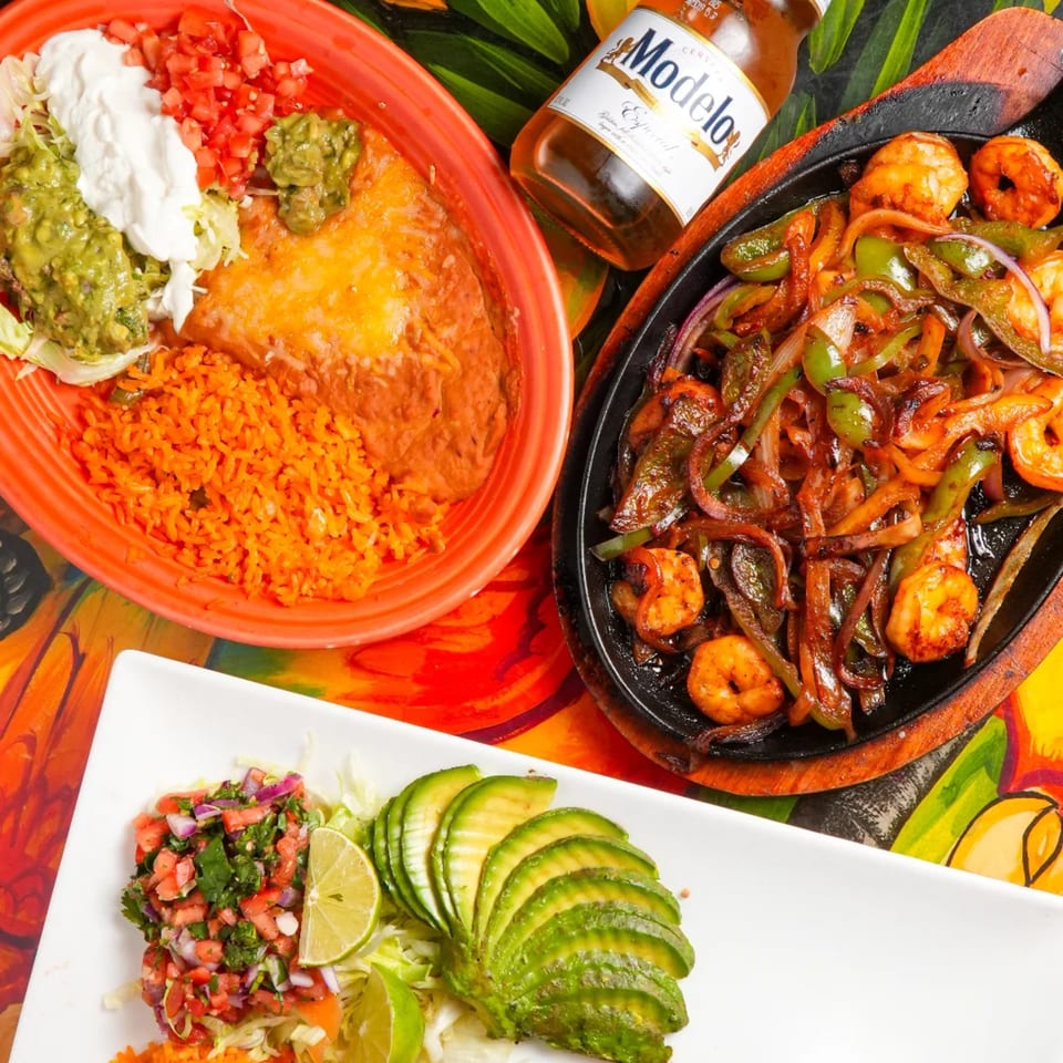 Los Magueyes Mexican Restaurant's fajitas, rice, beans, and a Modelo beer on a colorful table.