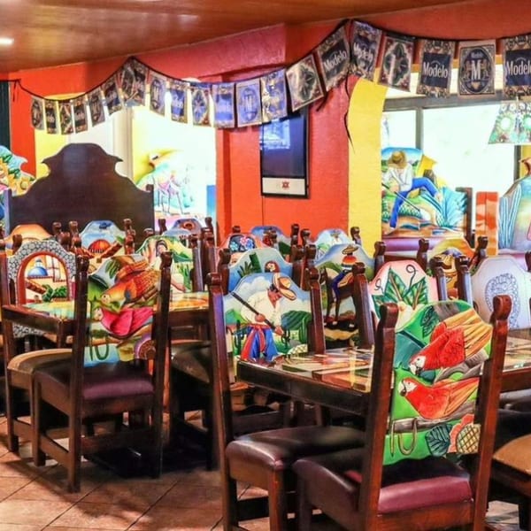 Vibrant Mexican restaurant interior with brightly painted chairs, red walls, and Modelo banners.