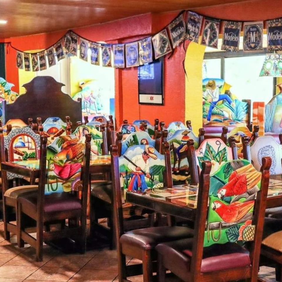 Vibrant Mexican restaurant interior with brightly painted chairs, red walls, and Modelo banners.