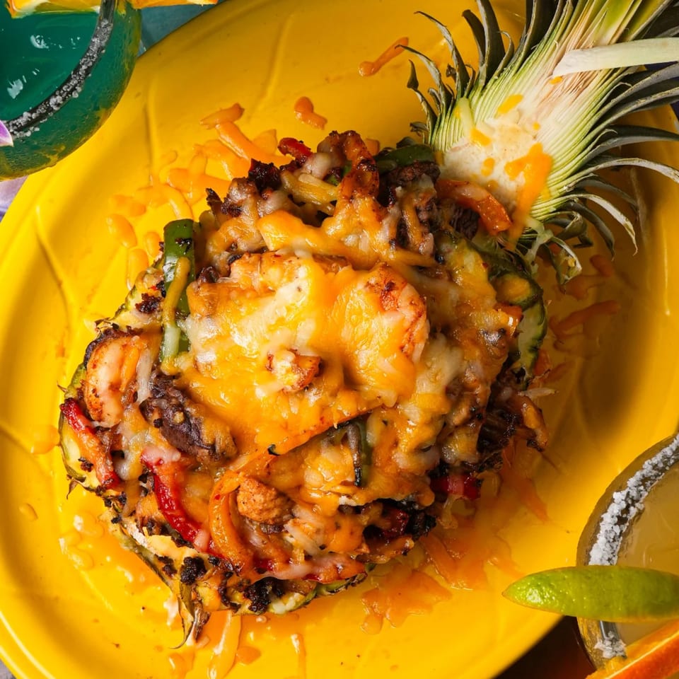 Cheesy pineapple fajitas with shrimp and vegetables, served on a yellow plate with a margarita.