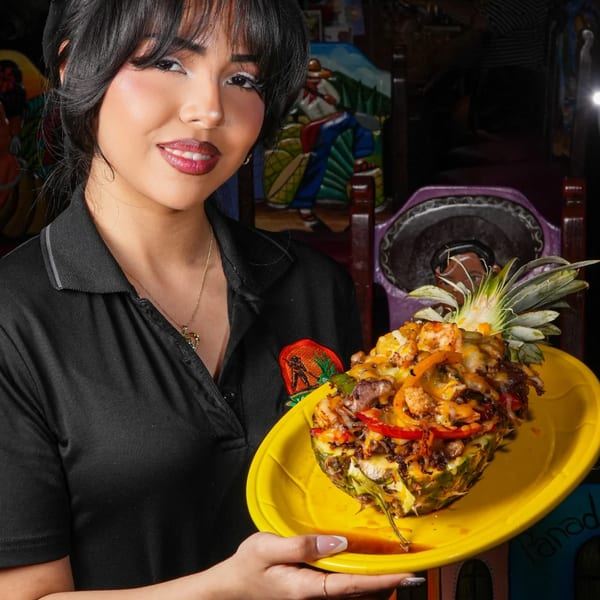 A server at Los Magueyes holds a vibrant pineapple filled with grilled meat, peppers, and cheese.