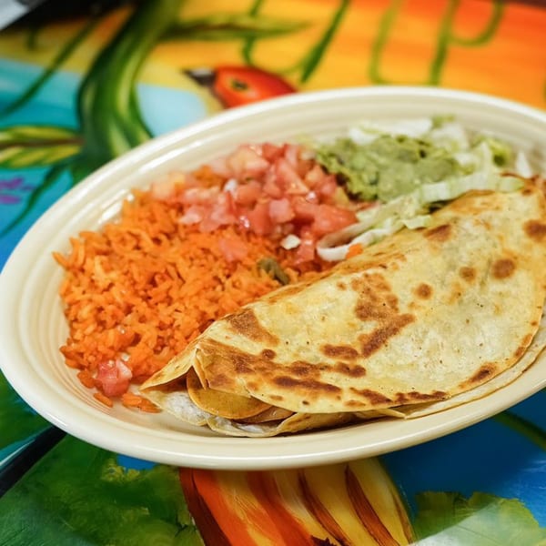 A quesadilla, rice, pico de gallo, and guacamole on a plate from Los Magueyes Mexican Restaurant.