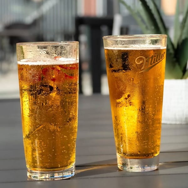 Two frosty glasses of golden beer, one with a Miller logo, on a dark outdoor table.