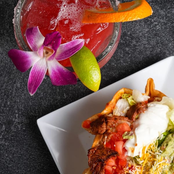 Overhead view of a vibrant red margarita with an orchid and a taco salad.