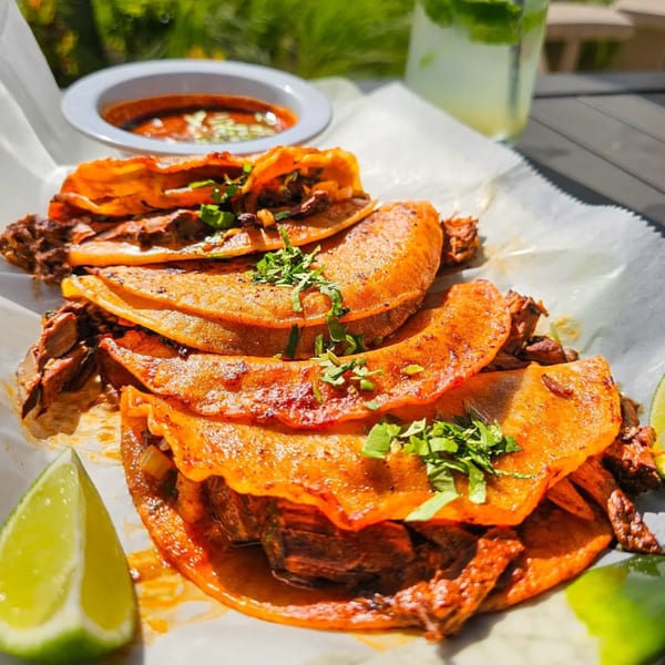 Los Magueyes birria tacos with cilantro and lime, served with a side of consommé.