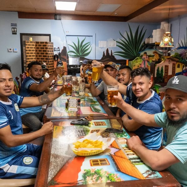 Group of men toasting with beers at a colorful table in Los Magueyes Mexican Restaurant.