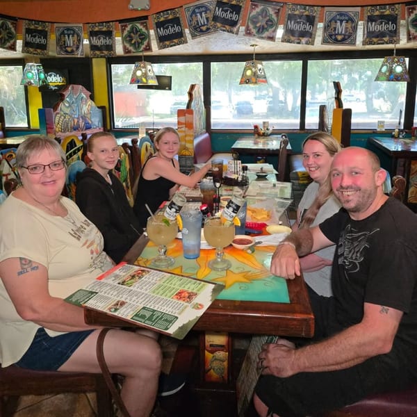 A family of five smiles at a table with drinks and menus at Los Magueyes Mexican Restaurant.