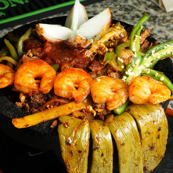 Molcajete with shrimp, steak, peppers, onions, and red sauce in a black bowl.